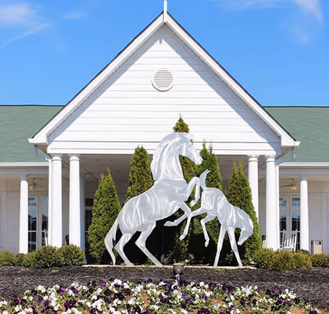 White horse sculptures in front of the columned entrance of a white building with landscaped flowers.