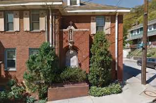 A brick senior living facility exterior with an entrance, greenery, and a small niche statue.