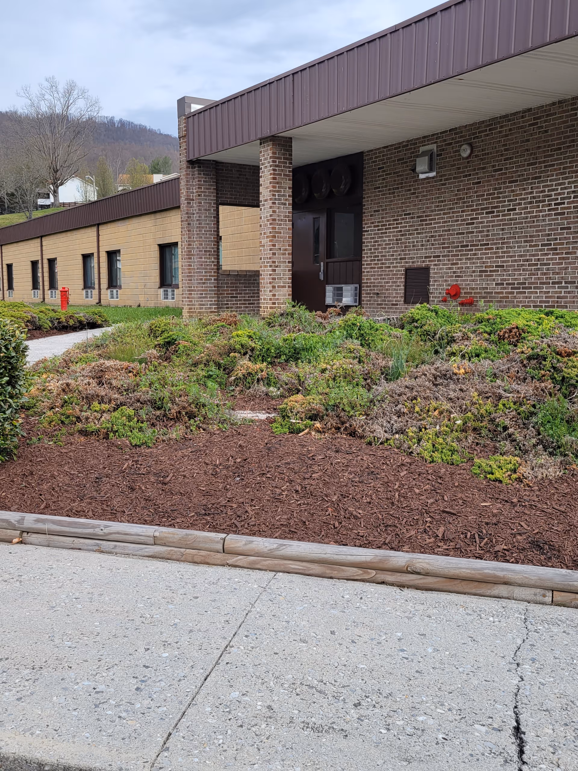 Entrance and front facade of a one-story brick assisted living building with landscaped beds and a sidewalk.