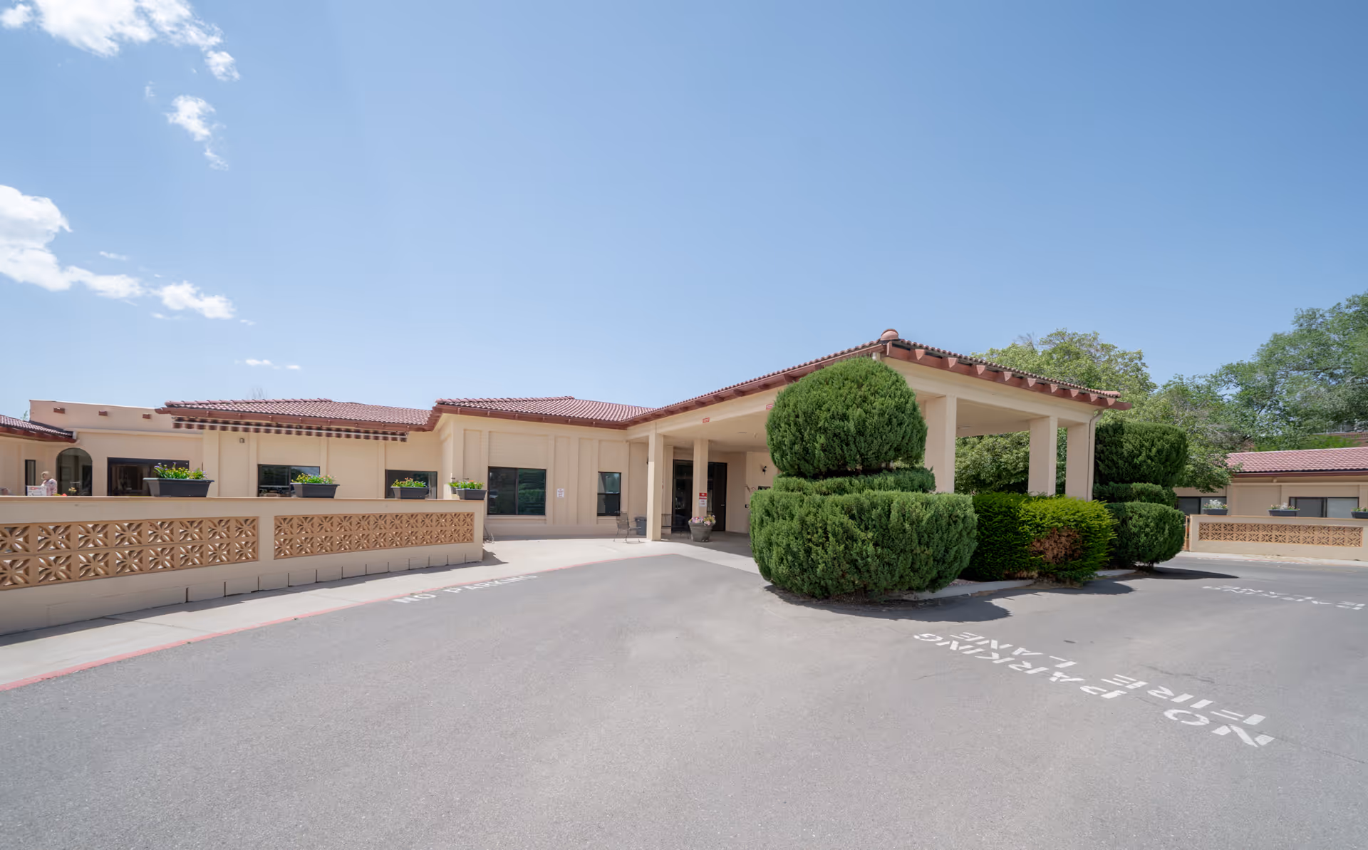 Exterior view of La Villa Grande Care Center showing a single-story building with a covered entrance, neatly trimmed bushes, and a clear blue sky.