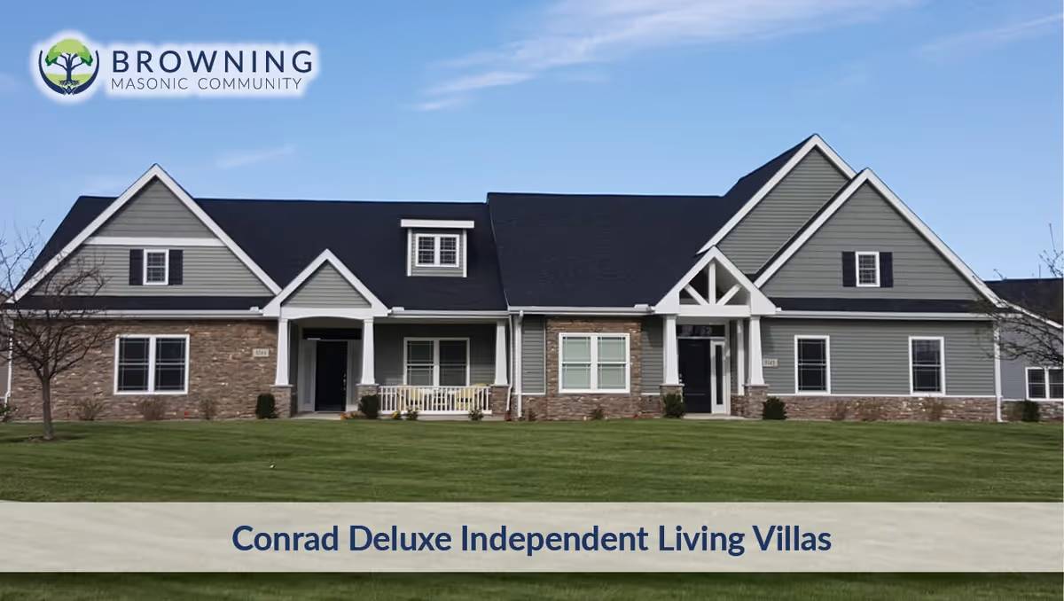 Exterior view of a single-story residential building with gray siding, stone accents, multiple windows, and two front entrances under a clear blue sky. The building is surrounded by a well-maintained green lawn.