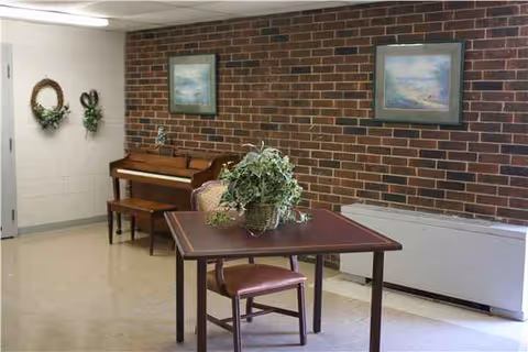Interior common room with brick wall, piano, table, and framed art.