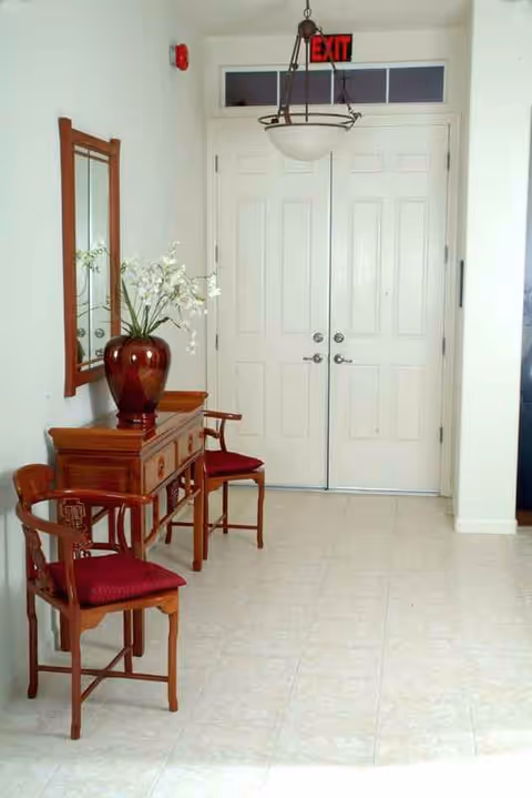 Interior hallway with double doors, a wooden console, mirror, chairs, and a vase.