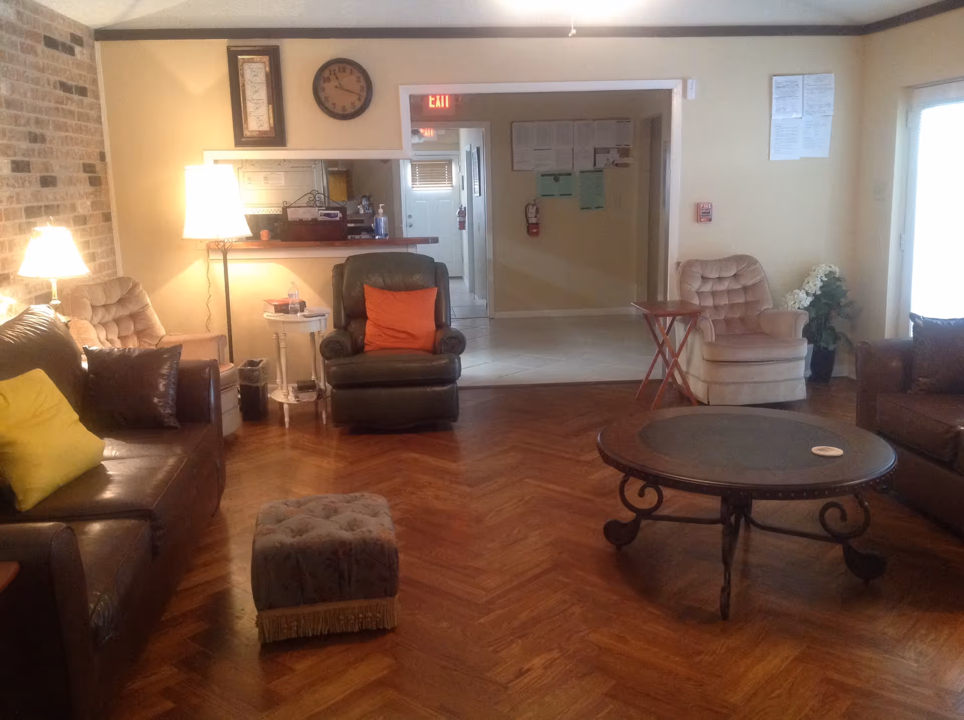 A cozy living room with sofas, armchairs, a round coffee table and lamps on a herringbone wood floor.
