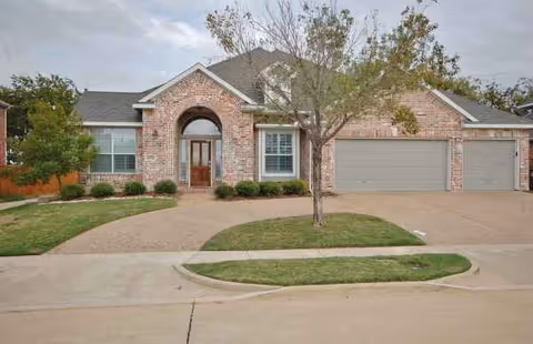Brick suburban house exterior with a tree, driveway, and attached two-car garage.