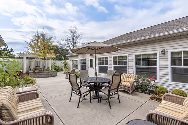 Outdoor patio with table, chairs, umbrella, and Brookdale Troy building exterior.