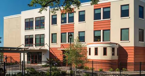 Exterior view of St Margaret's Daughters Home building with red accents and fencing.
