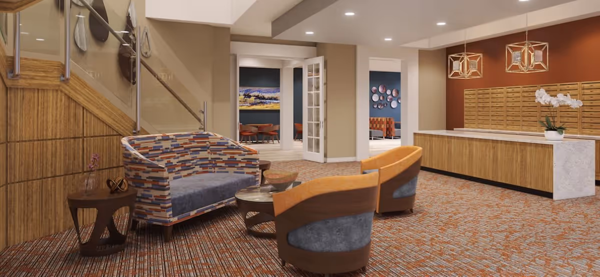 Modern senior living lobby with patterned seating, two orange chairs, a reception desk with mailboxes, and a staircase.