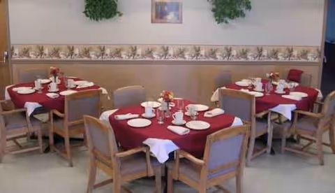 Senior living dining room with red tablecloths and neatly arranged place settings on round tables.