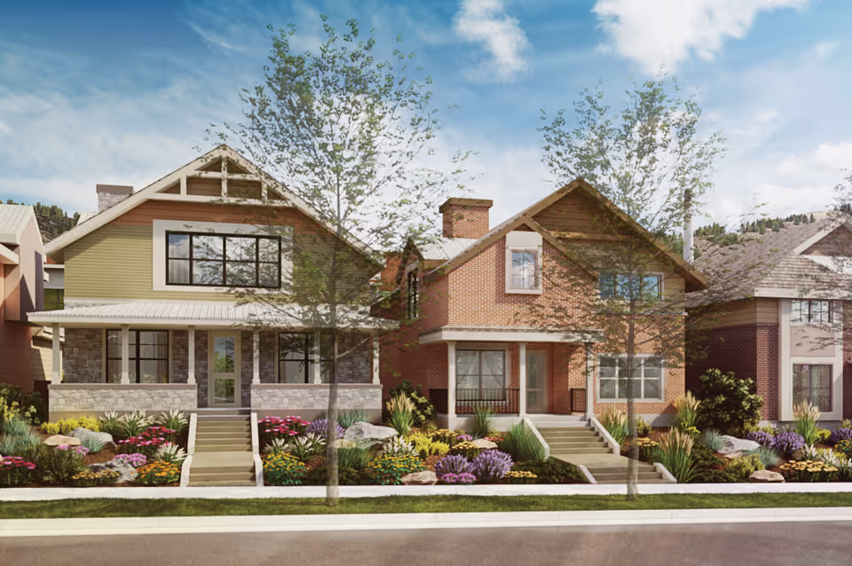 Front view of two two-story craftsman-style homes with porches, landscaped flower beds, and young street trees under a blue sky.