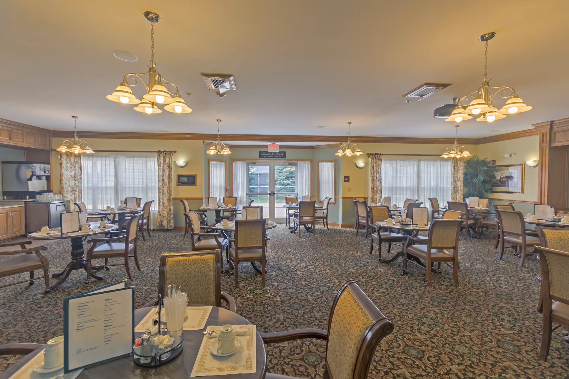 Spacious, well-lit communal dining room with multiple set tables and chairs, chandeliers, and patterned carpet.