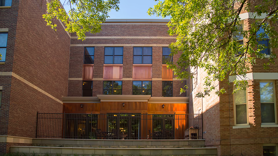 Brick exterior of a three-story courtyard facade with large windows, a fenced ground-level patio, and overhanging trees.