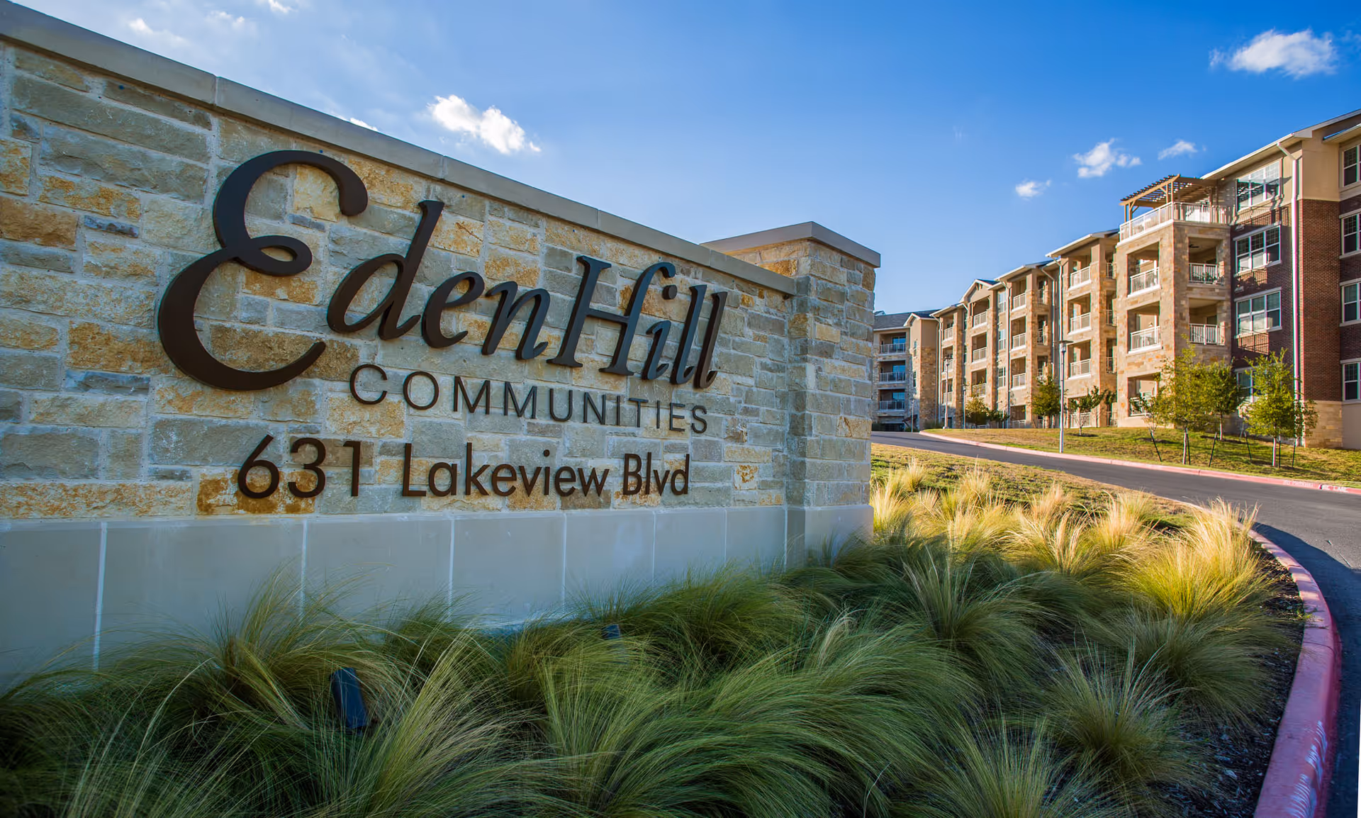 Stone sign for EdenHill Communities at 631 Lakeview Blvd with a multi-story residential building and landscaped greenery in the background under a blue sky.