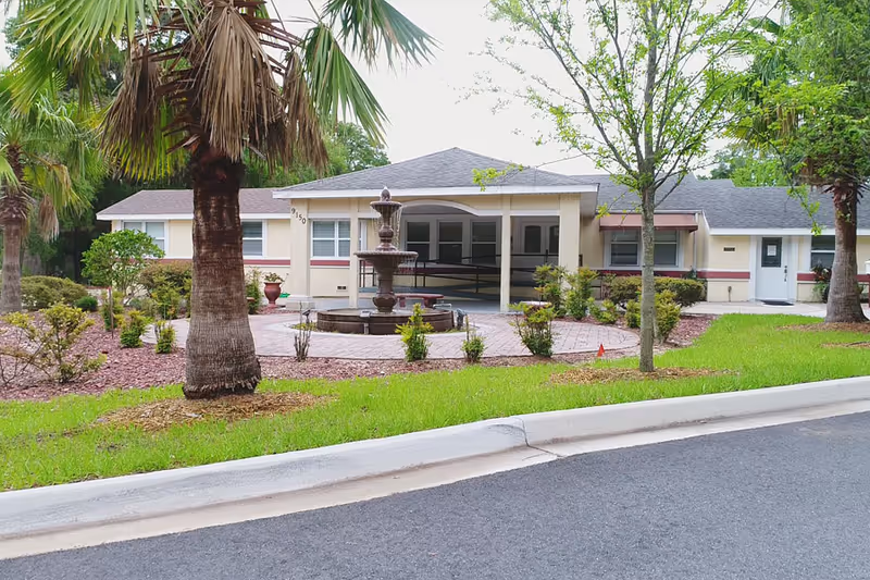 Exterior of Her Heart Gardens Assisted Living with a central fountain, landscaping, and palm trees.
