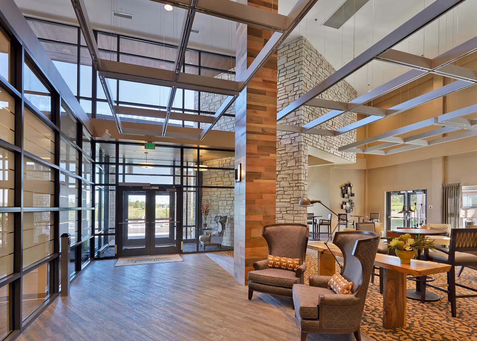 Spacious modern lobby with tall glass entrance, stone accent walls, and a seating area of armchairs and tables.