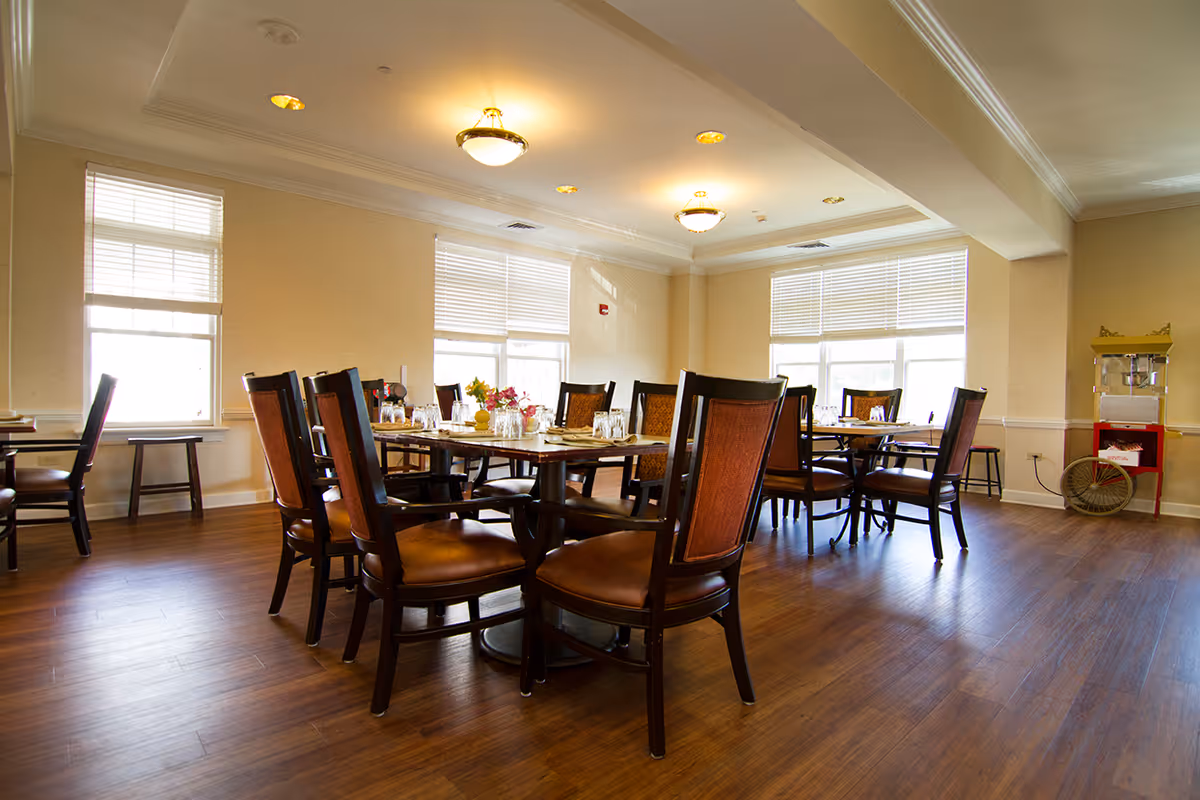 Bright dining room with wooden tables and chairs set for a meal and large windows letting in daylight.