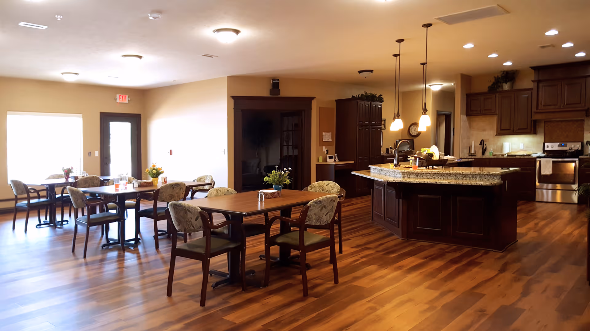 Spacious communal dining area with multiple tables and chairs and an open kitchen featuring a large island and pendant lights.