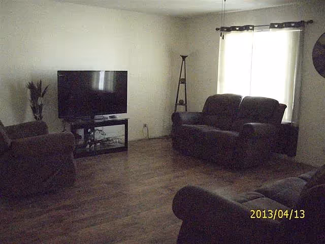 Spacious living room with dark sofas and armchairs, a TV on a stand, wood flooring, and a curtained window.