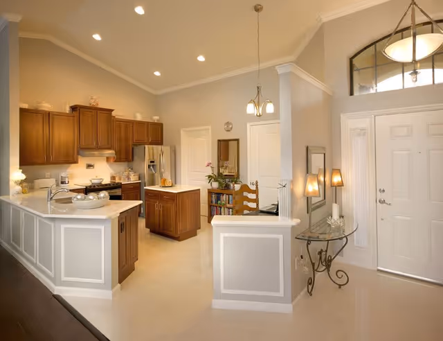 Bright open kitchen and entryway with white countertops, wooden cabinets, an island, and pendant lights.