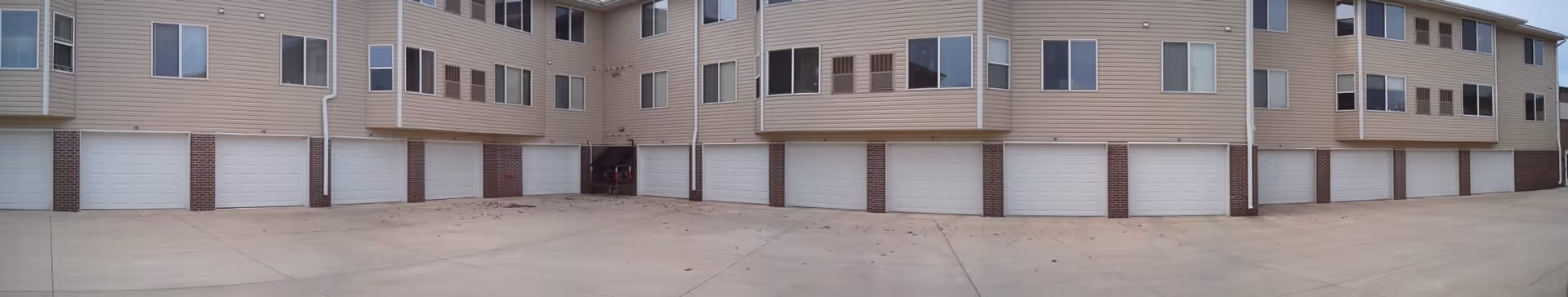 Panoramic view of a multi-unit building exterior showing a row of ground-level garage doors beneath upper-floor apartment windows.