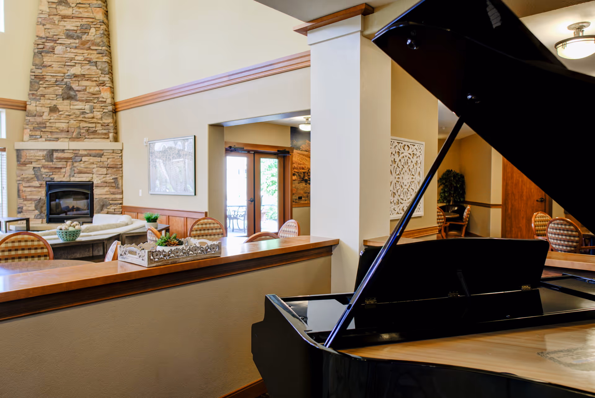 Interior common lounge with a grand piano in the foreground and a seating area with a stone fireplace in the background.