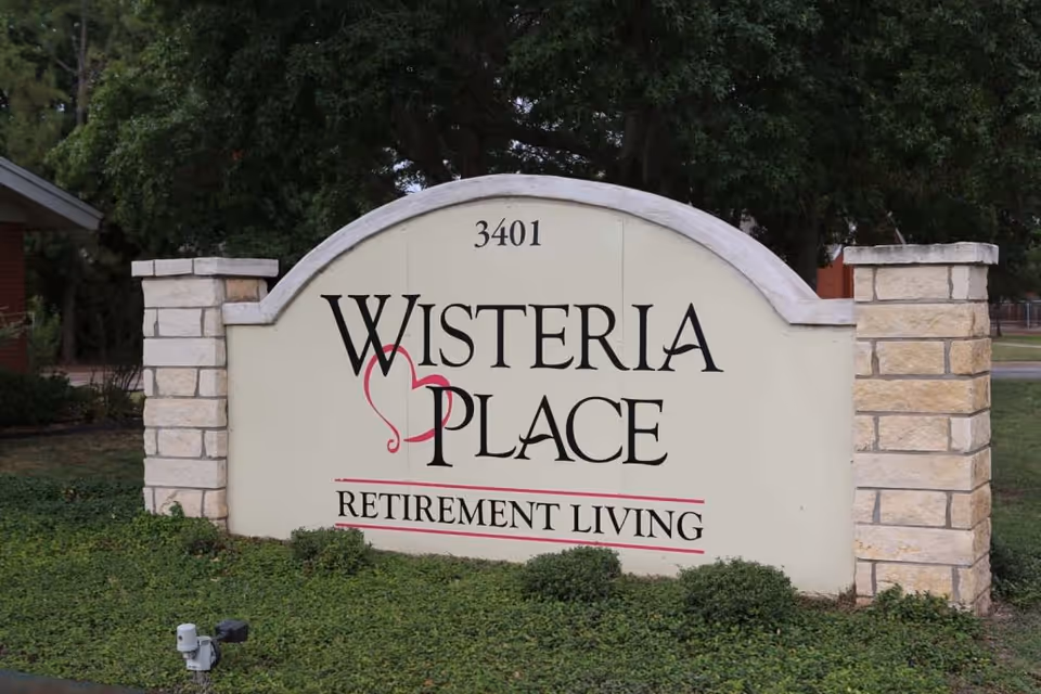 Stone-framed entrance sign reading "Wisteria Place Retirement Living" with the address 3401 and surrounding landscaping.