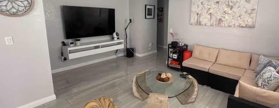 Modern living room with a wall-mounted TV, glass coffee table, and beige sectional.