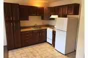 Small kitchenette with dark wood cabinets, a white refrigerator and stove, a sink, and a tiled linoleum floor.
