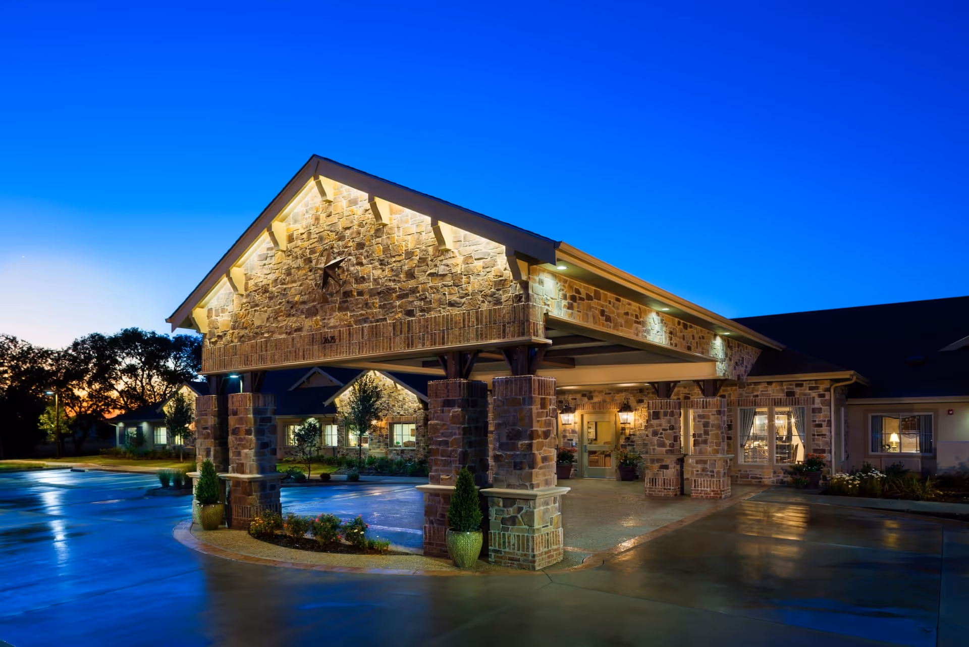 Stone-faced covered entrance with pillars and warm lighting at a senior living facility during twilight.