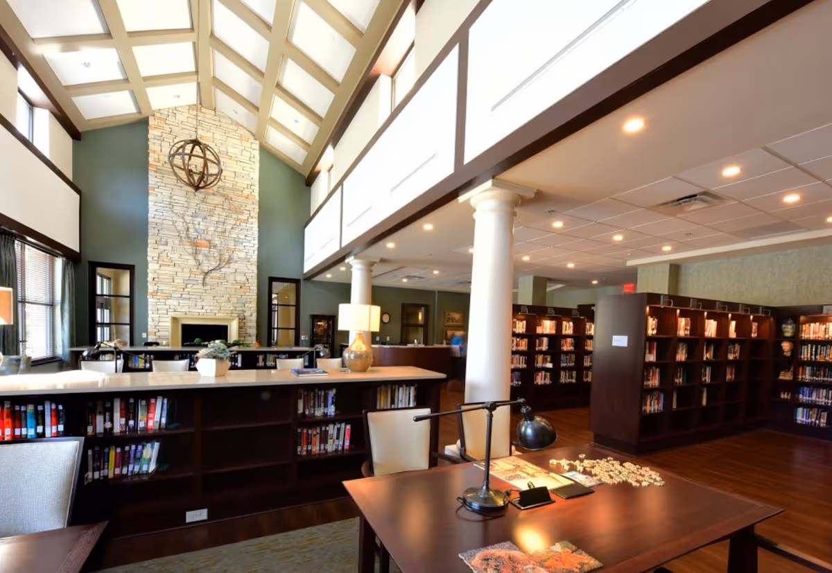 Bright two-story library/common room with a vaulted skylight ceiling, stone fireplace, bookshelves and reading tables.