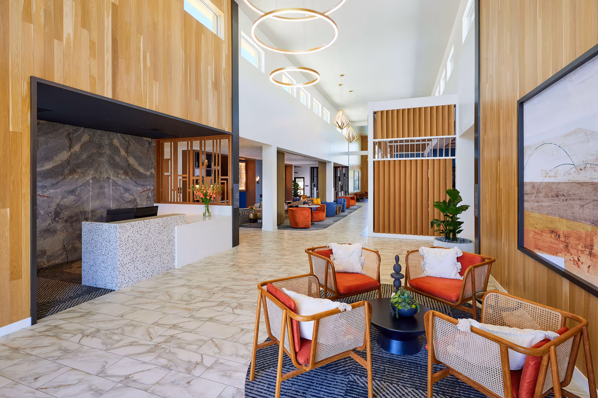 Bright modern lobby with a reception desk, high ceilings and a seating area of wicker chairs with red cushions.