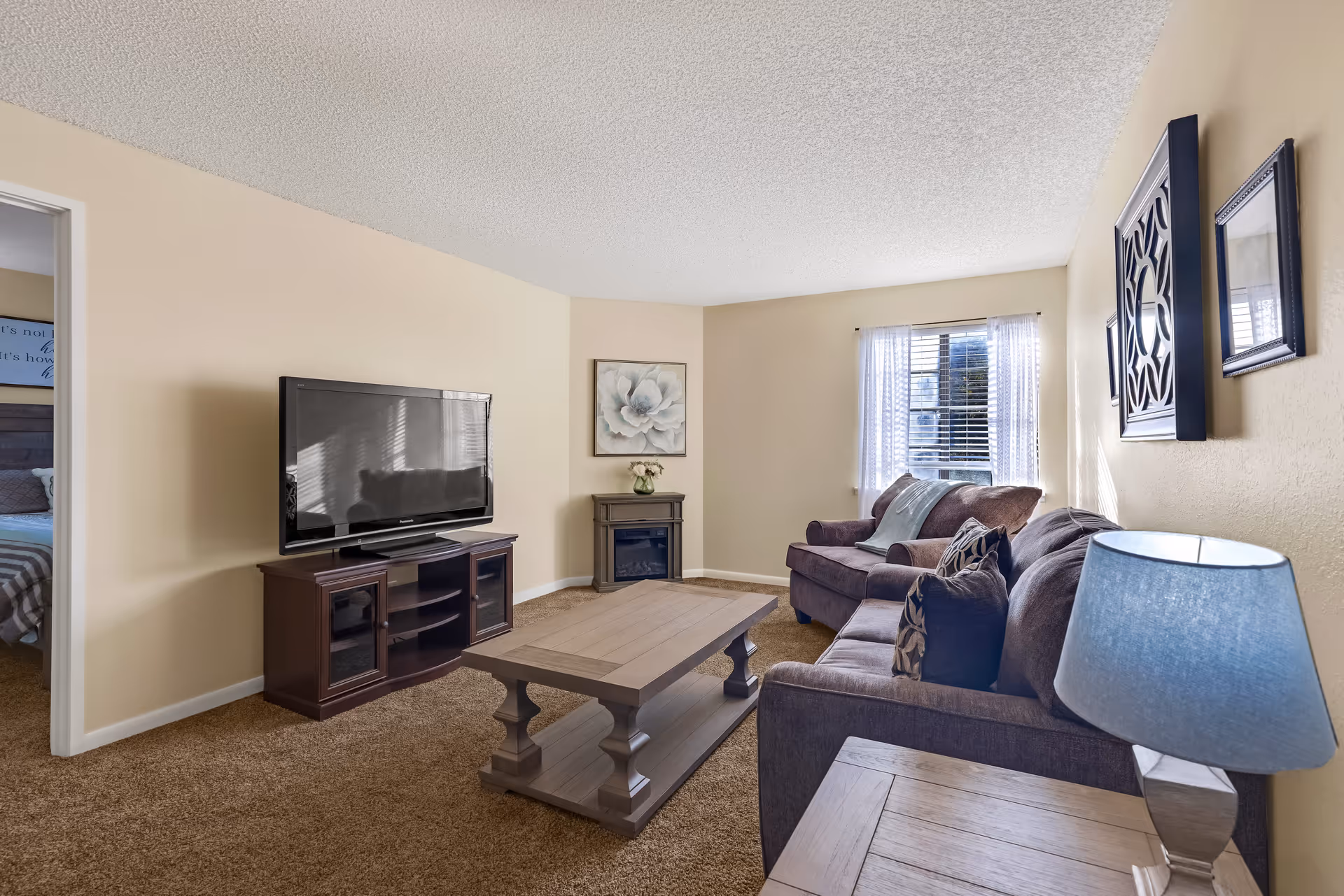 Well-lit living room with a sofa and armchair, coffee table, TV on a stand, and a side lamp.