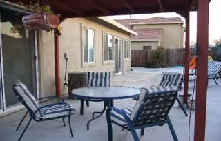 Outdoor patio with round table and striped chairs in a fenced residential area.