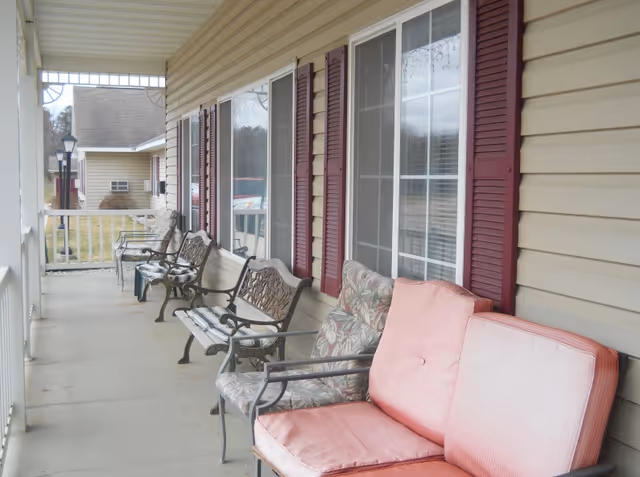 Covered porch with a row of metal and cushioned chairs along the exterior windows of a residential building.
