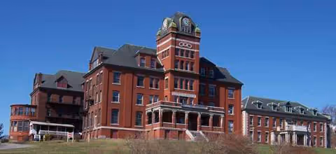 Brick senior living facility with a prominent clock tower on a grassy lawn.