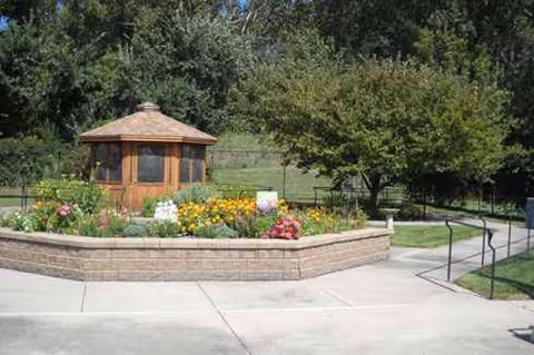 Outdoor courtyard at Cottagewood Senior Communities featuring a wooden gazebo surrounded by flowers.