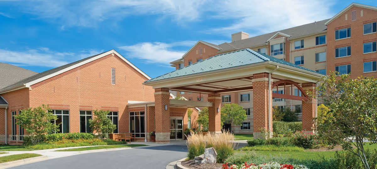 Exterior view of Riderwood senior living facility with brick buildings, a covered entrance, and landscaped grounds.