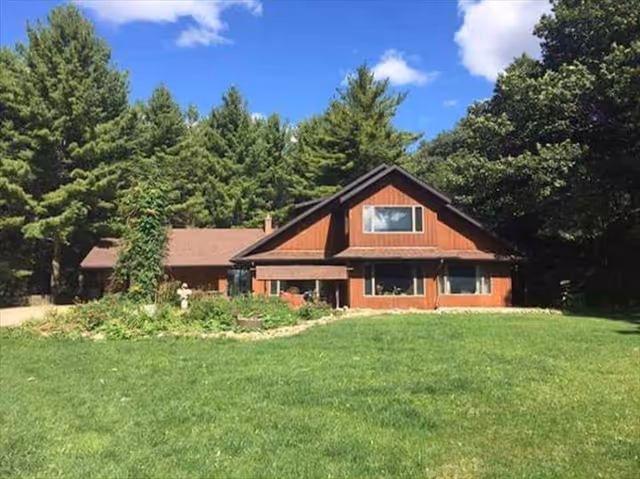 Brown two-story lodge-style building with a large grassy front lawn and trees under a blue sky.