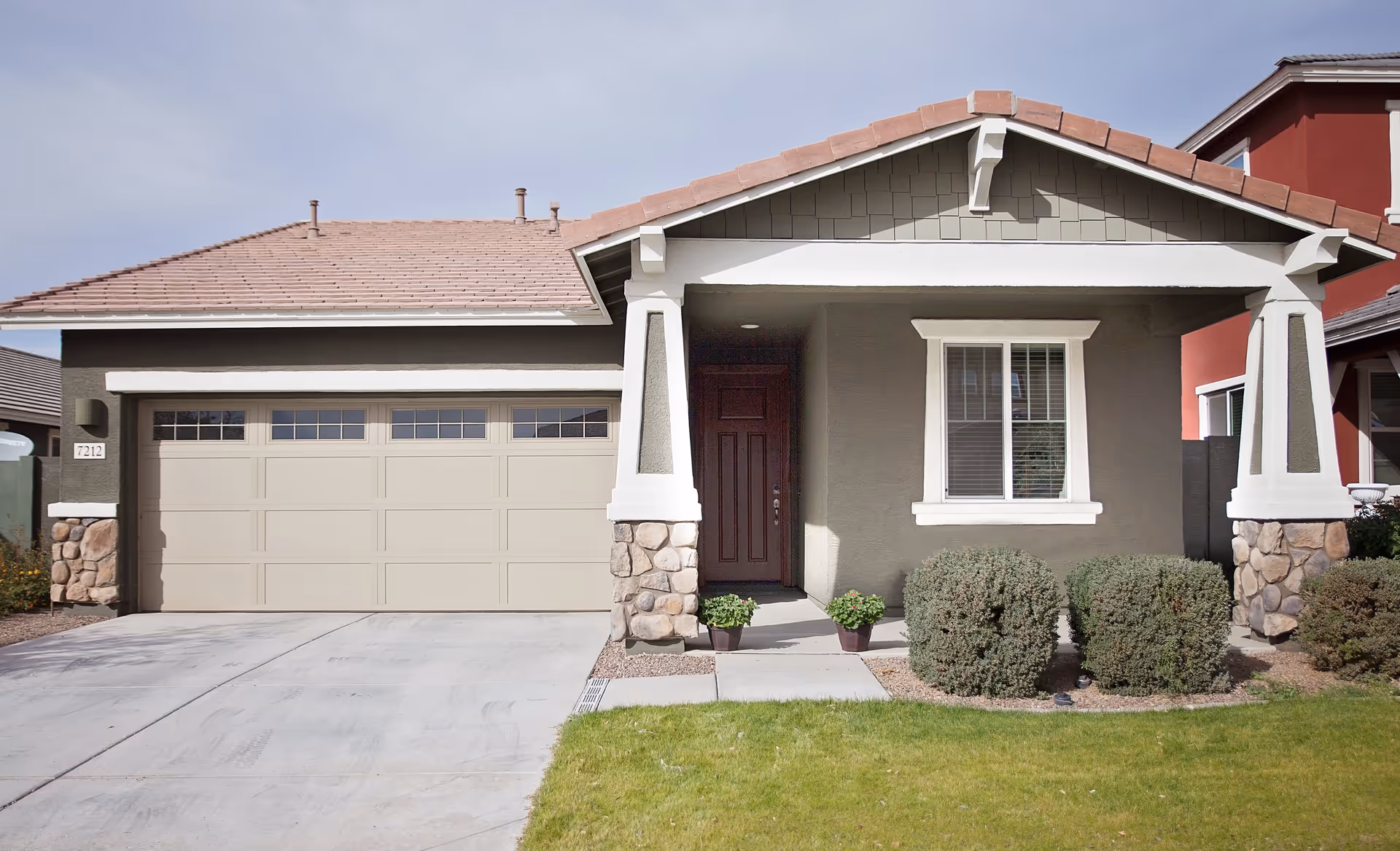 Front exterior of a single-story house with a two-car garage, covered porch, and shrubs in the yard.
