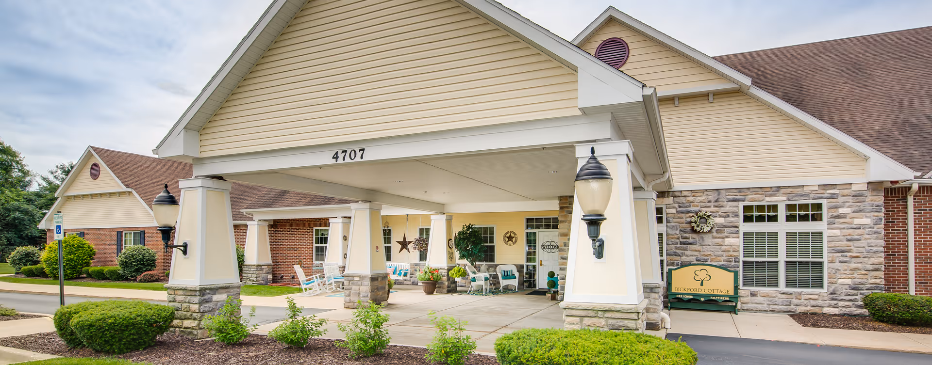 Covered front entrance of Bickford of Portage, a senior living facility, with pillars and chairs.