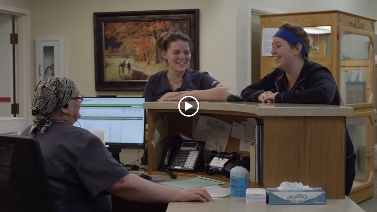 Three staff members chatting across a reception desk inside a senior care facility.