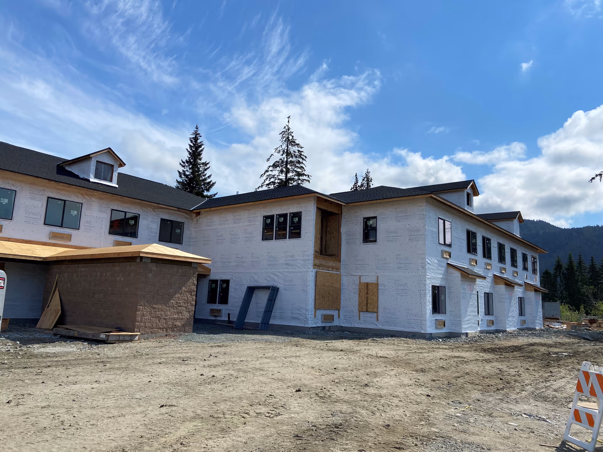 Two-story senior living building under construction with white weather wrap, pitched roofs, and a dirt lot in the foreground.