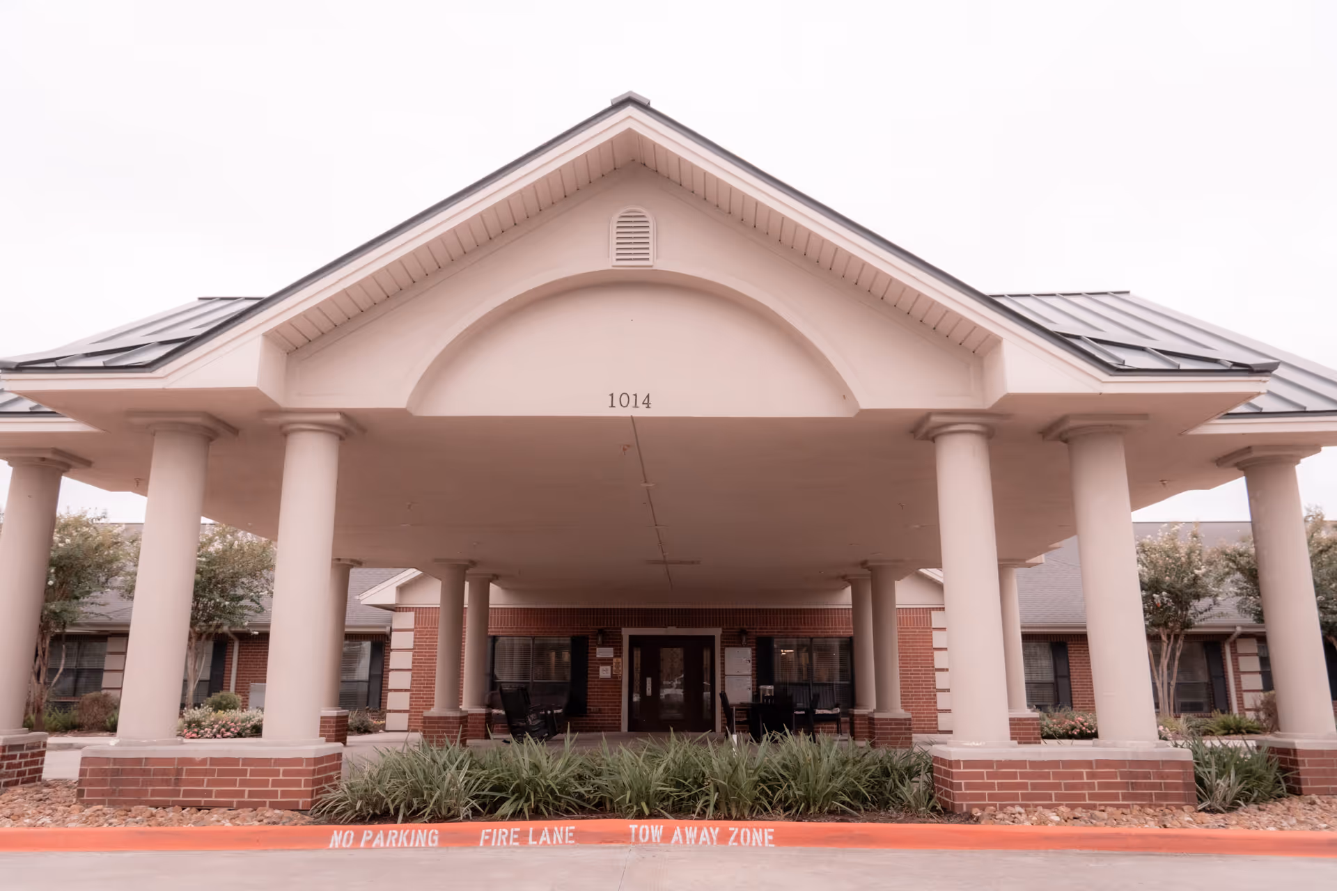 Covered front entrance (porte-cochere) with columns, brick facade and double doors under a gabled roof marked "1014".
