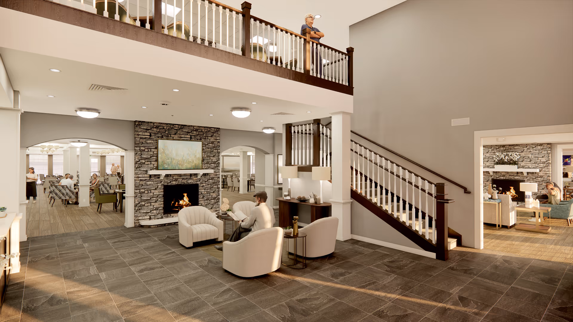 A spacious senior living facility common area with a stone fireplace, three beige armchairs arranged around a small table, and a staircase leading to an upper balcony where an elderly person is standing. The room has gray tiled flooring and light gray walls. In the background, there are dining areas with people seated at tables.