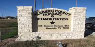 Stone sign with nursing and rehabilitation text, flanked by pillars, in front of a parking lot.