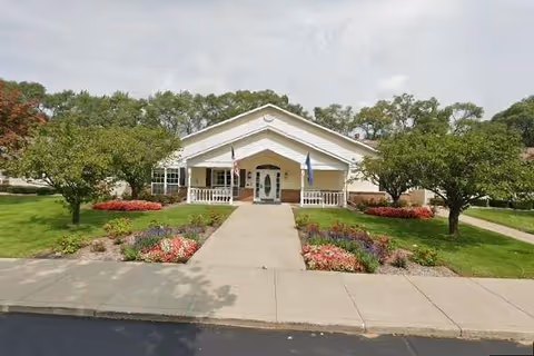 Exterior view of Dodge Park AIS building entrance with manicured lawn, trees, and flower beds.