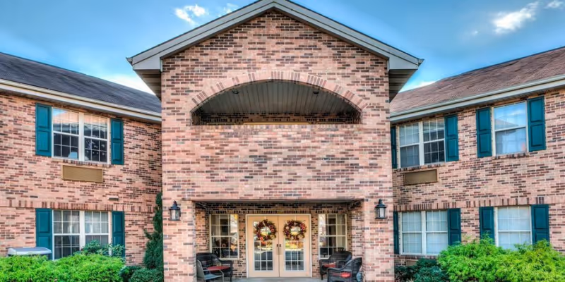 Front entrance of a two-story brick senior living building with double glass doors decorated with wreaths and exterior seating.