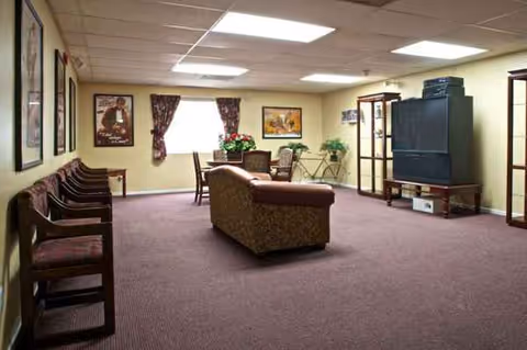 A quiet senior living common area with seating, a couch, TV, and potted plants.