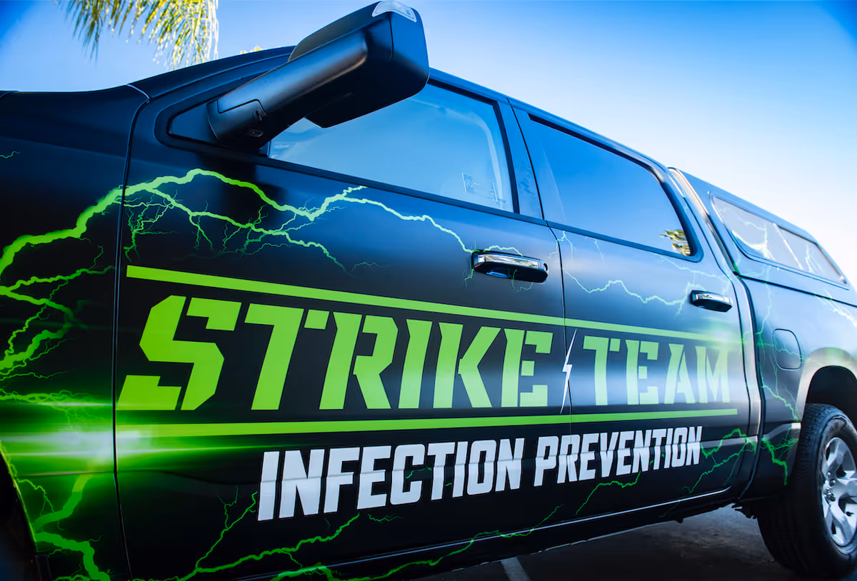Black pickup truck parked outdoors with large green lettering reading "STRIKE TEAM" and "INFECTION PREVENTION" and green lightning graphics on the side.
