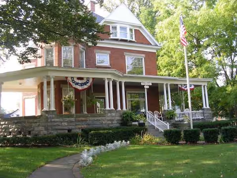 Red brick senior living home with wraparound porch and flag outside.